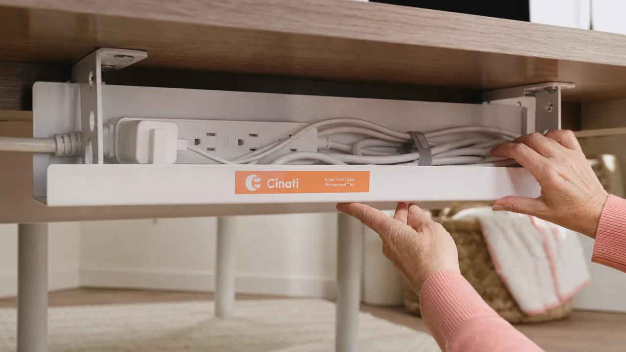 Under-desk view showing a white cable tray holding a power strip and multiple organized cables out of sight
